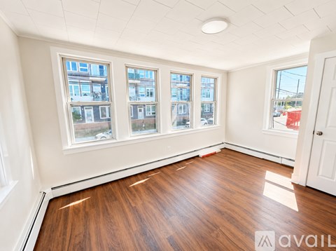 A room with wooden floors and three windows overlooking a street.