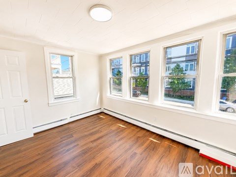 A room with wooden floors and white walls has a window with a view of a building and trees.