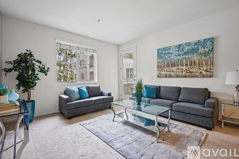 A living room with a grey couch, a glass coffee table, and a painting on the wall.