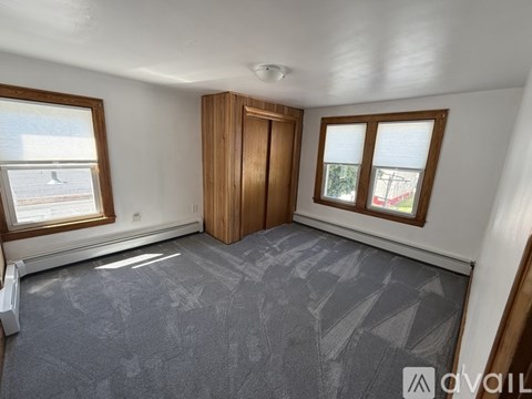A room with a carpeted floor, a wooden door, and two windows with blinds.