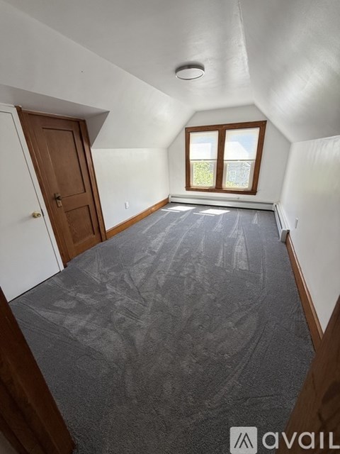 A room with a carpeted floor and a window with a view of a fence.