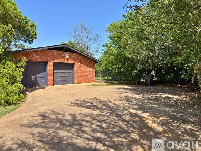 A red brick building with a grey garage door is surrounded by green trees.