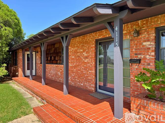 A red brick house with a porch and a green plant in front.