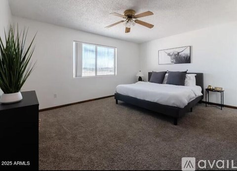 A bedroom with a bed, a ceiling fan, and a plant on a table.