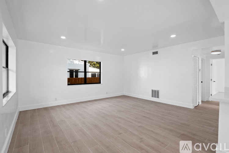 A spacious room with wooden flooring and a window with a view of trees and a building.