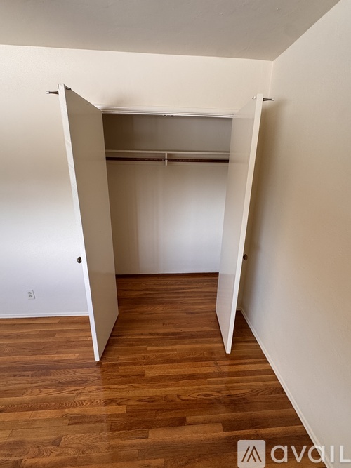 A room with a wooden floor and a white wall with a doorway leading to another room.
