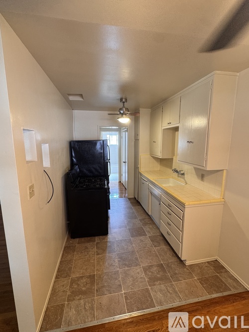 A kitchen with a black fridge, white cabinets, and a tiled floor.