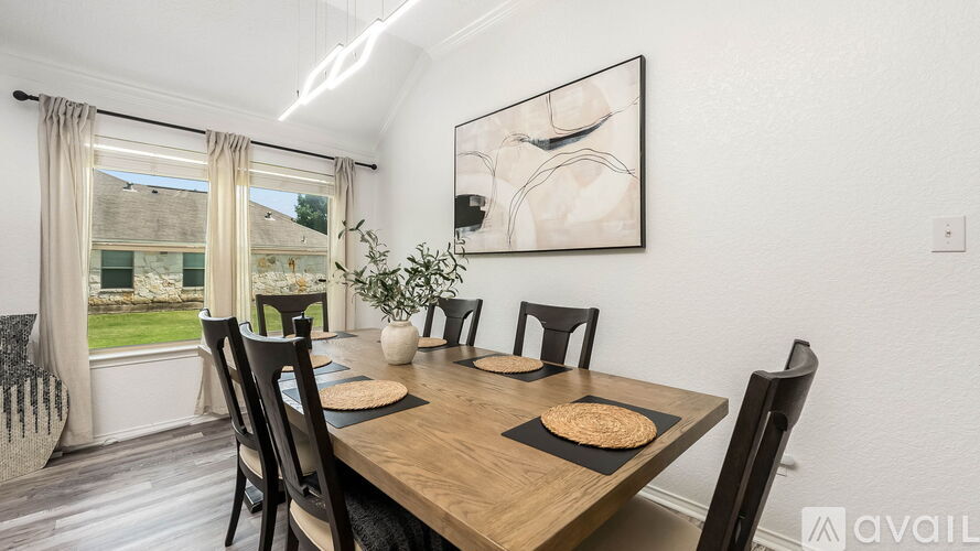 A dining room with a wooden table and chairs, a framed artwork on the wall, and a view of a lawn through the window.
