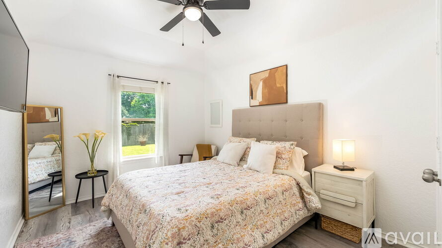 A bedroom with a large bed, a ceiling fan, and a window with a view of greenery outside.