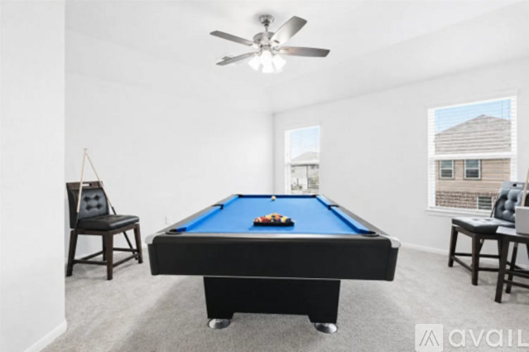 A pool table is in the middle of a room with a ceiling fan and two chairs.