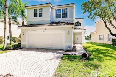 A two-story house with a white garage door is surrounded by a well-manicured lawn and palm trees.