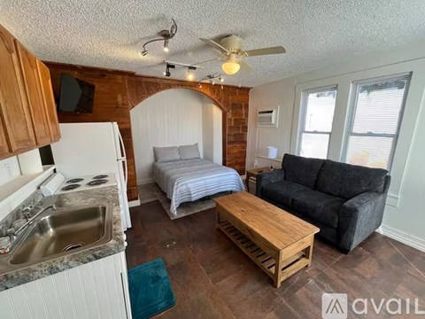 A kitchen with a refrigerator, sink, and a living room with a couch and a bed.