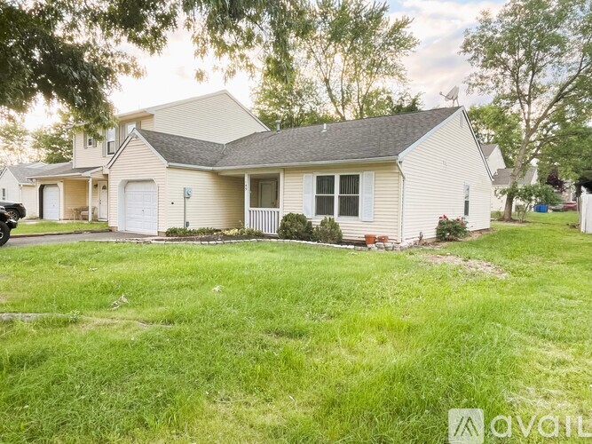 A house with a white exterior and a grey roof is surrounded by a green lawn.