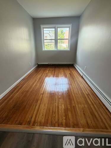 A room with wooden flooring and a window showing a view of a building outside.
