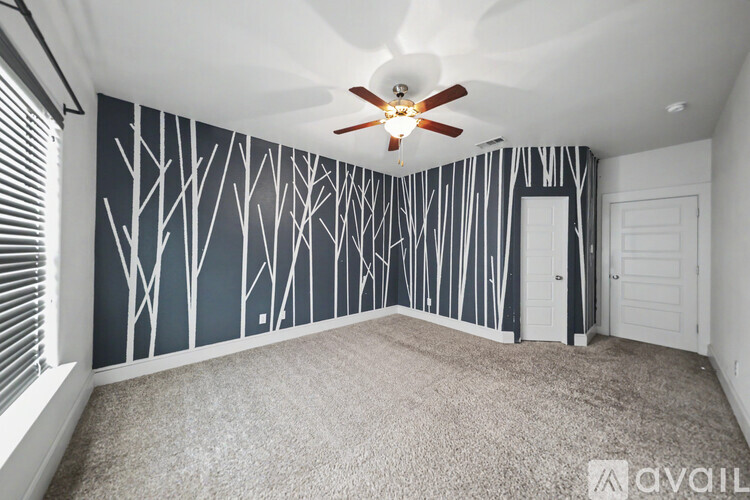 A room with a ceiling fan and a wallpaper design of trees.