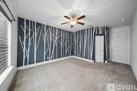 A room with a ceiling fan and a wallpaper design of trees.