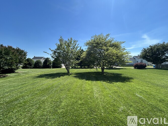 A grassy field with two trees and a house in the background.