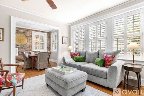 A living room with a grey couch, a wooden chair, a table with a lamp and a fan on the ceiling.