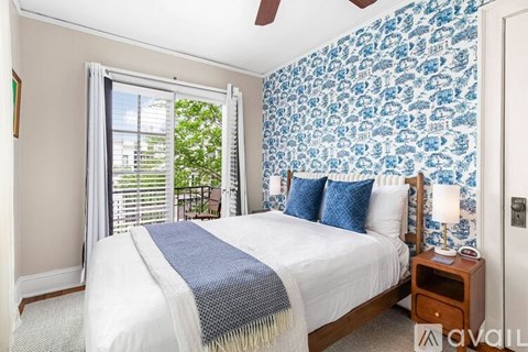 A bedroom with a bed, a nightstand, and a window with blinds.