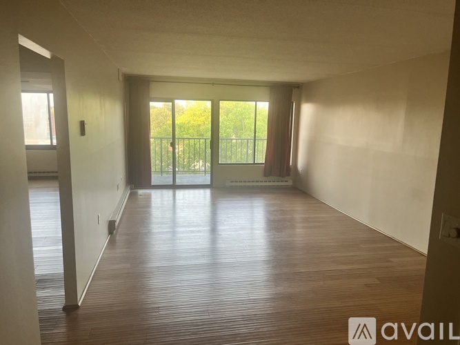 A spacious room with wooden flooring and a view of a green fence through the glass doors.