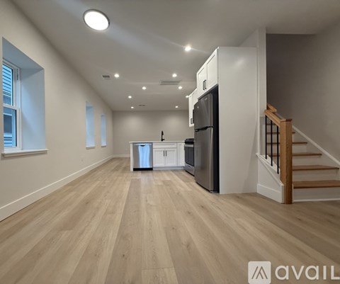 A kitchen with a refrigerator, oven, and stove in a spacious room with wooden flooring and a staircase in the background.
