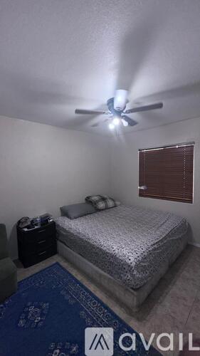 A bedroom with a bed, a ceiling fan, and a window with blinds.