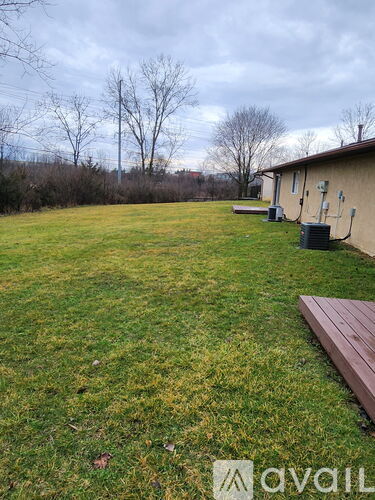 A grassy backyard with a wooden bench and a house in the background.