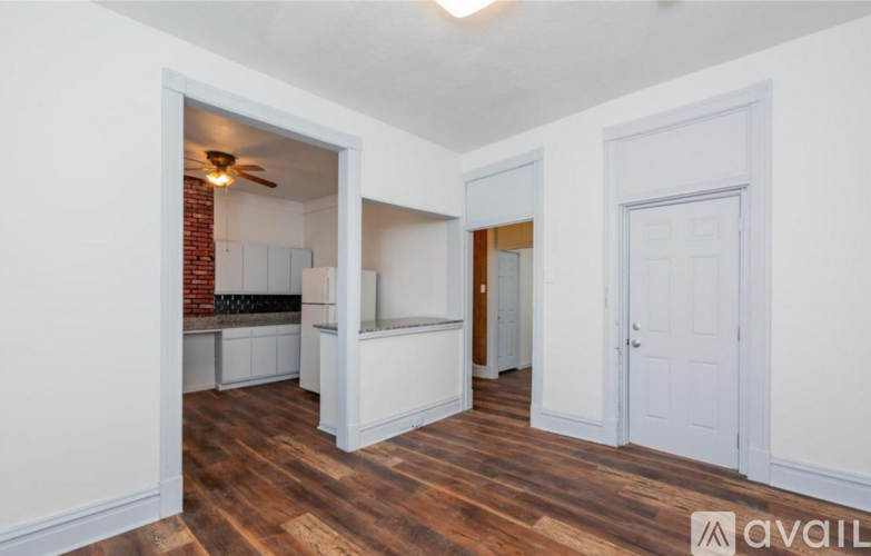 A room with wooden floors and white walls, with a doorway leading to another room.