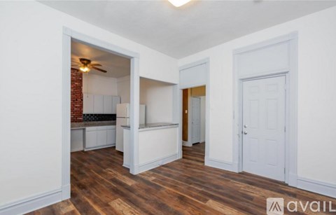 A room with wooden floors and white walls, with a doorway leading to another room.