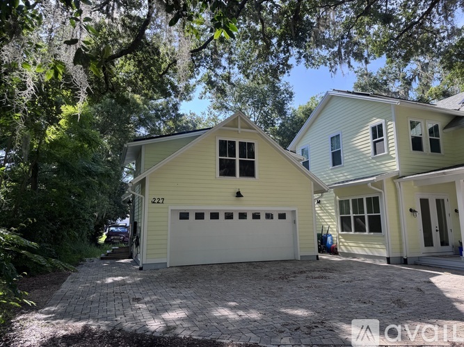 A yellow house with a white garage door is surrounded by trees.