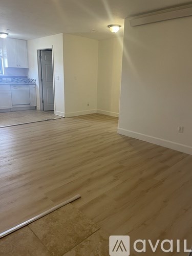 A room with wooden flooring and a kitchen area in the background.