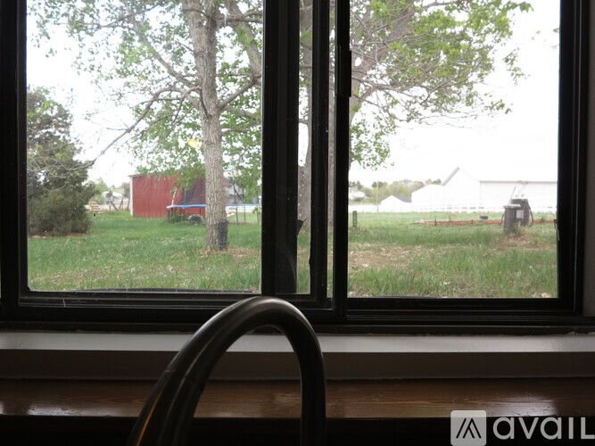 A window with a view of a tree, a red building, and a tractor in the distance.