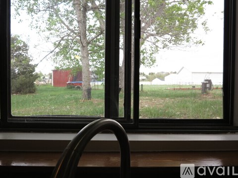 A window with a view of a tree, a red building, and a tractor in the distance.