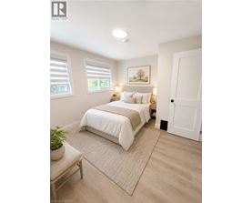 A bedroom with a bed, a nightstand, a window with blinds, a rug, a potted plant, and a painting on the wall.