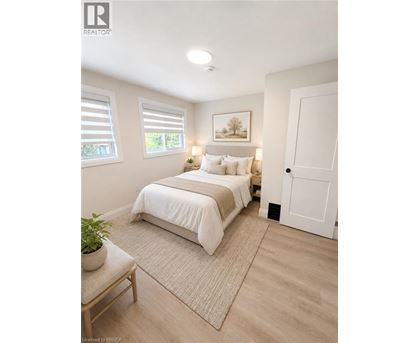 A bedroom with a bed, a nightstand, a window with blinds, a rug, a potted plant, and a painting on the wall.