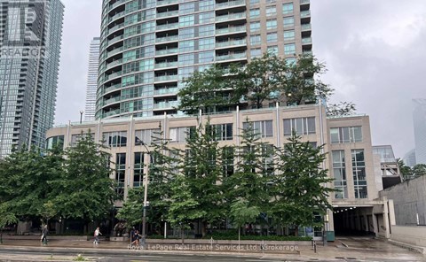 A modern building with a glass facade is surrounded by trees and other buildings.