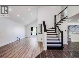 A spacious room with a wooden floor and a staircase with black railings.