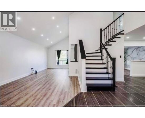 A spacious room with a wooden floor and a staircase with black railings.