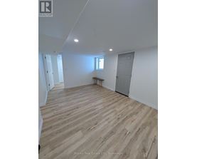 A room with wooden flooring and white walls, with a window and a door visible.