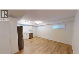A spacious room with wooden flooring and a kitchen area in the background.