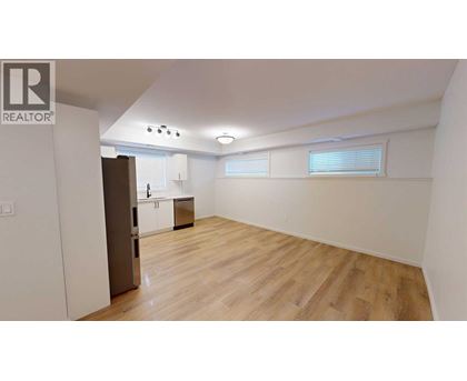 A spacious room with wooden flooring and a kitchen area in the background.