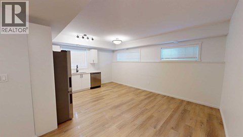 A spacious room with wooden flooring and a kitchen area in the background.