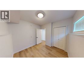 A room with wooden floors and white walls, with a door on the left and a window on the right.