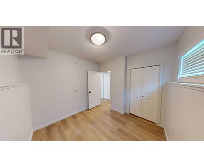 A room with wooden floors and white walls, with a door on the left and a window on the right.
