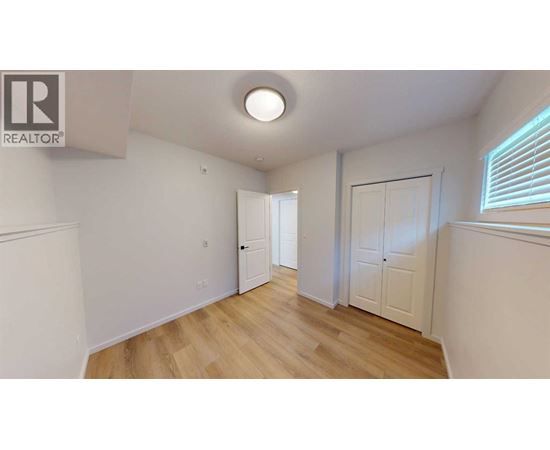 A room with wooden floors and white walls, with a door on the left and a window on the right.