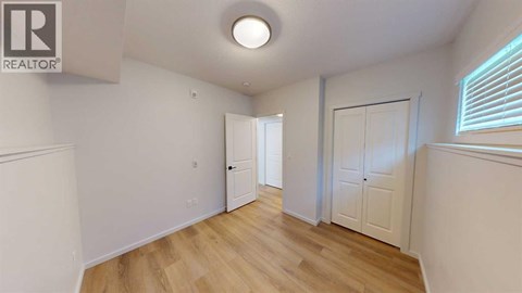 A room with wooden floors and white walls, with a door on the left and a window on the right.