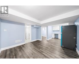 A spacious room with wooden flooring and a large refrigerator.