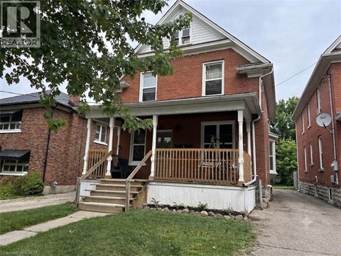 A red brick house with a porch and a tree in front.