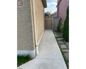 A concrete walkway leads to a wooden fence and a brick wall.