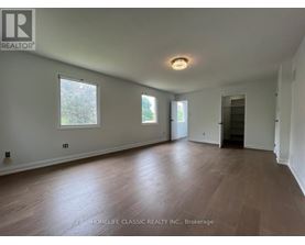 A room with wooden flooring and white walls, with a window on the left wall.